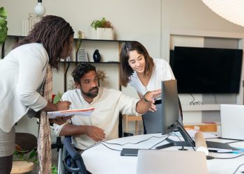 Three people discussing strategy in front of computer display.