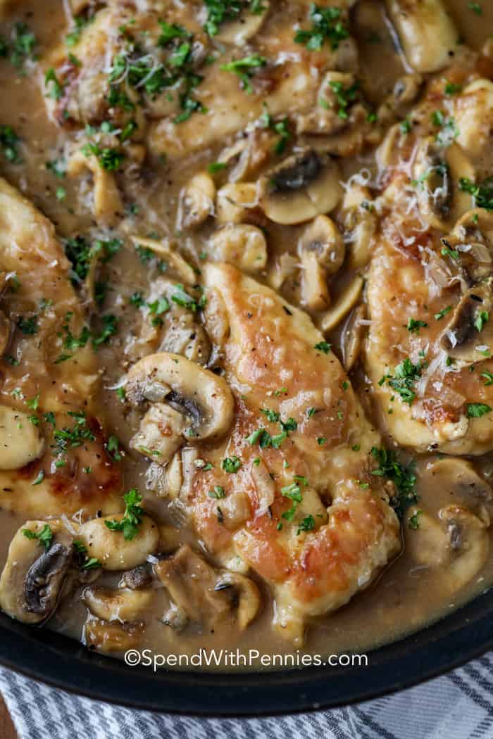 Chicken Marsala in a pan with mushrooms, parsley and shredded parmesan shown close up