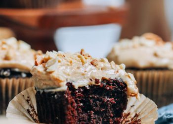 Partially eaten gluten-free chocolate cupcake topped with peanut butter frosting and chopped peanuts
