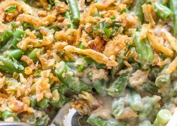 a cooked green bean casserole recipe in a white serving dish with a spoon
