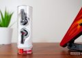 Nothing Ear Stick inside the case, vertically standing on a desk with plant and guitar