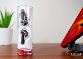 Nothing Ear Stick inside the case, vertically standing on a desk with plant and guitar